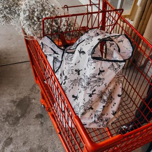Peut inclure: Un chariot de courses rouge avec un sac de courses r&eacute;utilisable blanc &agrave; motif noir et blanc de dragons et d'&eacute;toiles. Le sac est pli&eacute; et se trouve dans le chariot.