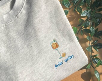 Sudadera bordada Feelin’ Spritzy, inspirada en el cóctel Spritz italiano. Cuello redondo.