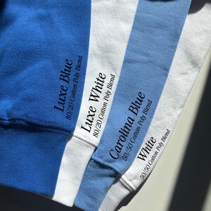 May include: Four fabric swatches in royal blue, white, light blue, and white. Text printed on the fabric reads: Luxe Blue 80/20 Cotton Poly Blend, Luxe White 80/20 Cotton Poly Blend, Carolina Blue 50/50 Cotton Poly Blend, and White 50/50 Cotton Poly Blend.