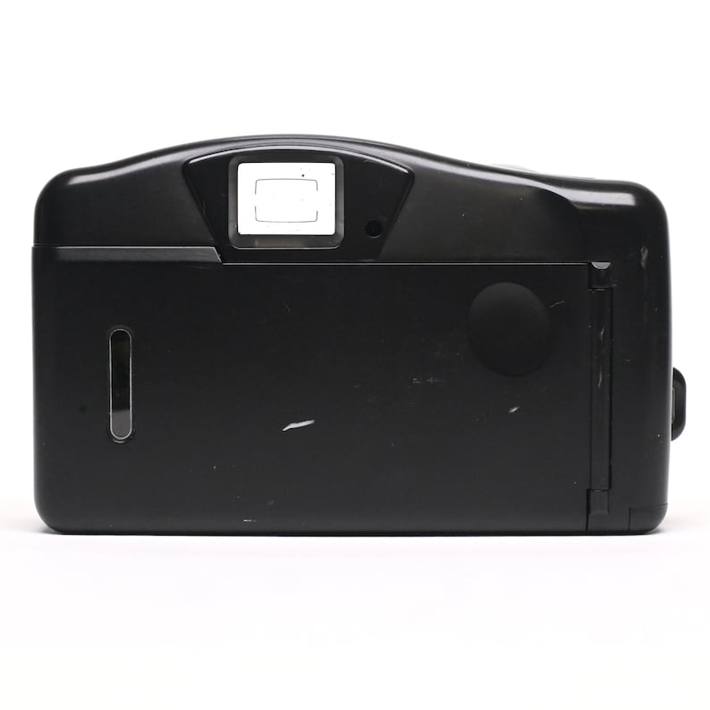 Pode incluir: C&acirc;mara de filme compacta preta com flash embutido. A c&acirc;mera tem um visor retangular e uma tampa de lente redonda.