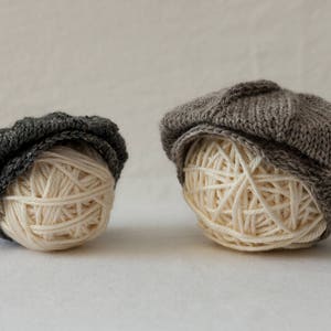 Peut inclure: Deux bonnets en tricot gris avec une pelote de laine à l'intérieur de chacun. Les bonnets sont de tailles et de styles différents.