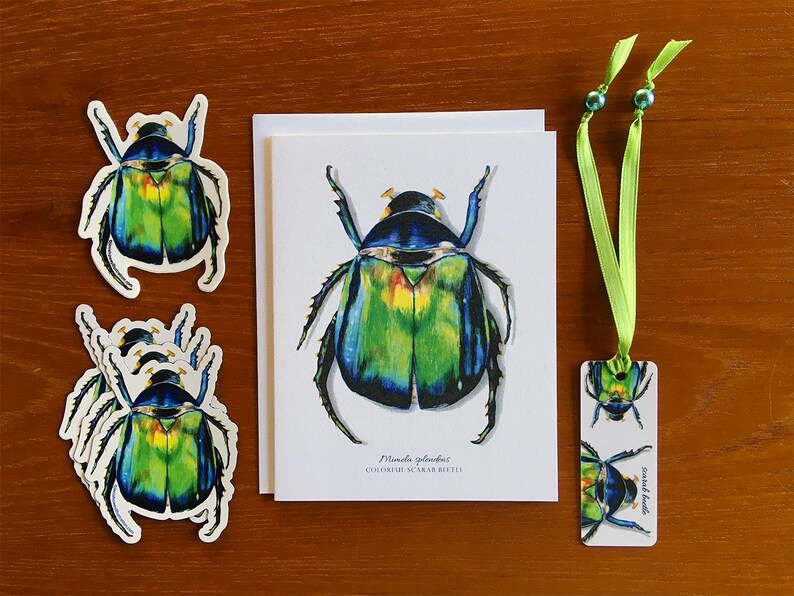 K&ouml;nnte beinhalten: Ein Satz gr&uuml;ner und blauer K&auml;fer-Aufkleber, eine Karte mit einer Illustration eines gr&uuml;nen und blauen K&auml;fers und ein Lesezeichen mit zwei K&auml;fer-Illustrationen. Die Karte tr&auml;gt den Text "Mimela splendens, Buntk&auml;fer".