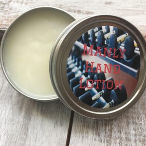 May include: A silver tin with a white label that says "MANLY HAND LOTION" in red letters. The label has a photo of a row of dumbbells in a gym.