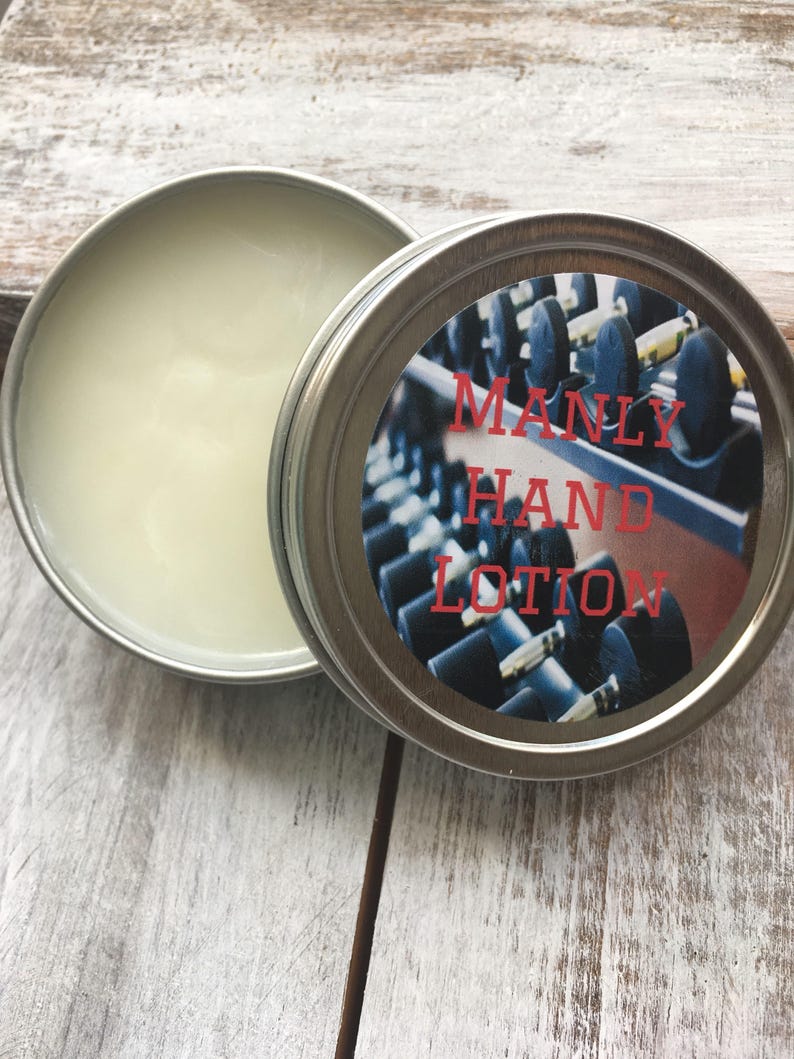 May include: A silver tin with a white label that says "MANLY HAND LOTION" in red letters. The label has a photo of a row of dumbbells in a gym.