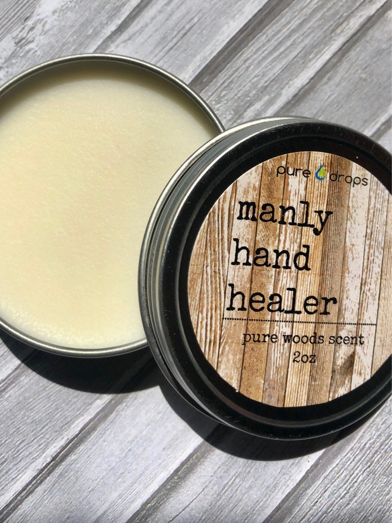 May include: A silver tin with a white label that reads "pure drops manly hand healer pure woods scent 2oz". The tin is open and contains a white balm.
