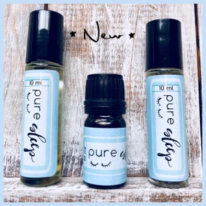 May include: Three glass bottles with black caps and labels that say "pure sleep" in white text. The bottles are 10 ml and are on a white wooden surface. The word "New" is written in black on the surface.