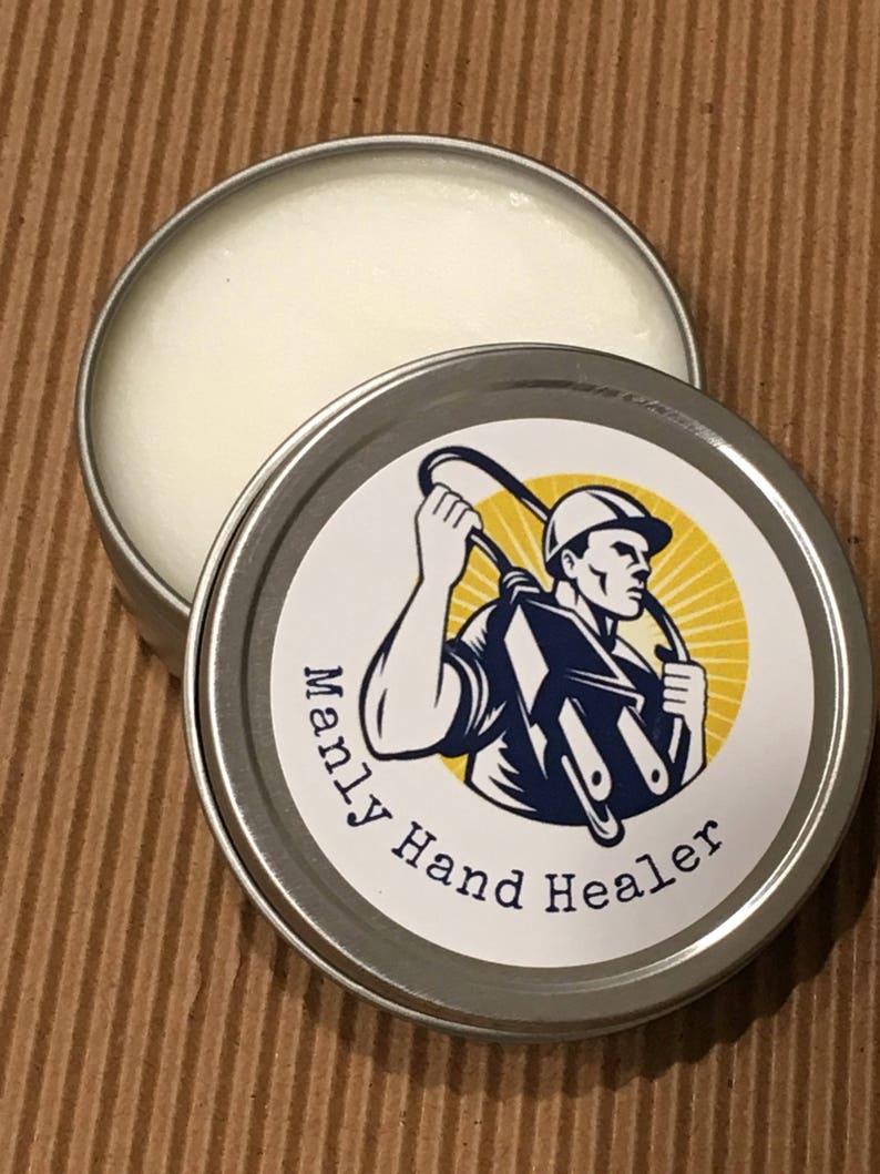 May include: A silver tin with a white label that says "Manly Hand Healer". The label features a cartoon illustration of a worker wearing a hard hat and holding a pair of pliers.