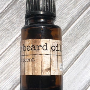 May include: A small amber glass bottle with a black cap. The bottle has a label that says "beard oil" and "scent".