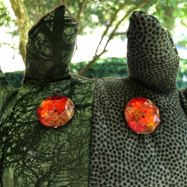 Peut inclure: Gros plan sur un jouet en peluche avec un tissu &agrave; motifs verts et bruns. Le jouet a deux gros boutons de gemmes rouges pour les yeux.