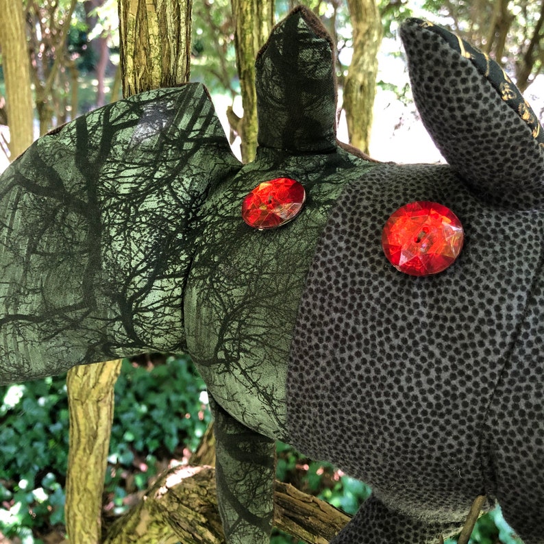 Peut inclure: Un jouet en peluche en forme de cr&eacute;ature avec un motif de camouflage et deux grands yeux en gemmes rouges.