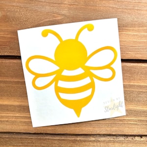 May include: A yellow bee sticker with a white background. The bee design features a round head, curved antennae, and striped body. The sticker has the text "Design by Starlight" in the lower right corner.