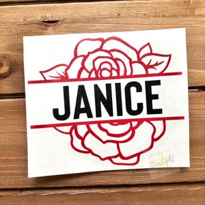 May include: A white sticker featuring the name "JANICE" in bold black letters, set against a red rose design. The design includes a horizontal red line above and below the name. The words "DESIGN BY Starlight" are in the bottom right corner.