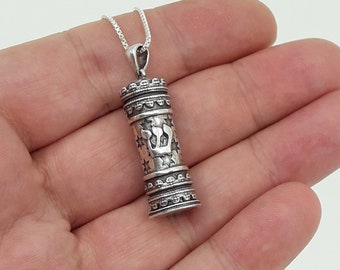 May include: A silver necklace with a silver pendant shaped like a scroll. The pendant is decorated with stars and a Hebrew inscription.