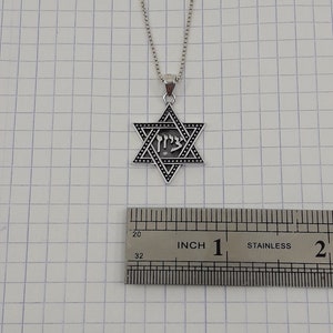 Puede incluir: Un collar de cadena de plata con un colgante de plata en forma de Estrella de David que presenta la palabra hebrea "Chai" en el centro. El colgante tiene un di&aacute;metro de aproximadamente 2,5 cm.