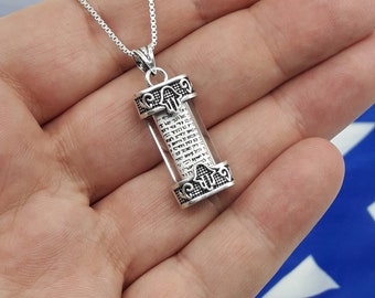 May include: A silver necklace with a clear glass pendant containing a scroll of Hebrew text. The pendant is decorated with a Hamsa hand design.