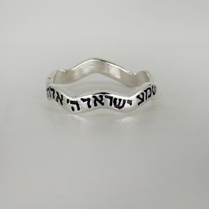 May include: A silver ring with a wavy band and Hebrew text inscribed on the outside.