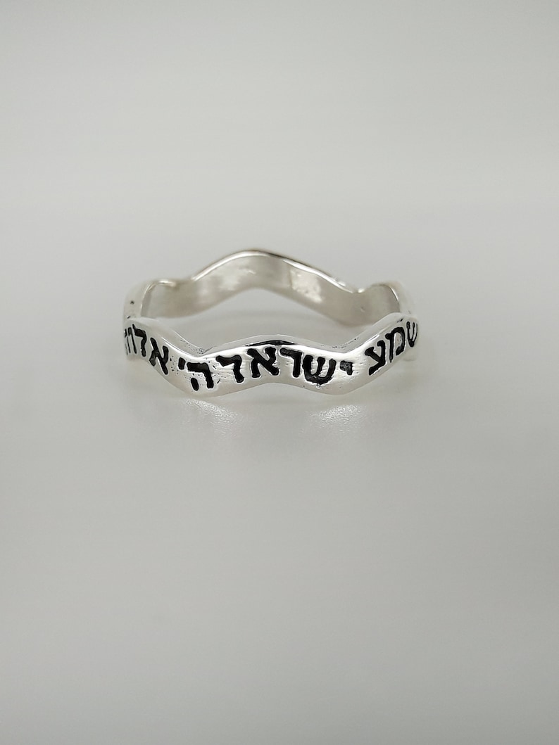 May include: A silver ring with a wavy band and Hebrew text inscribed on the outside.