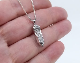 May include: A silver chain necklace with a small, silver pendant shaped like a cylinder. The pendant is covered in small, clear cubic zirconia stones.