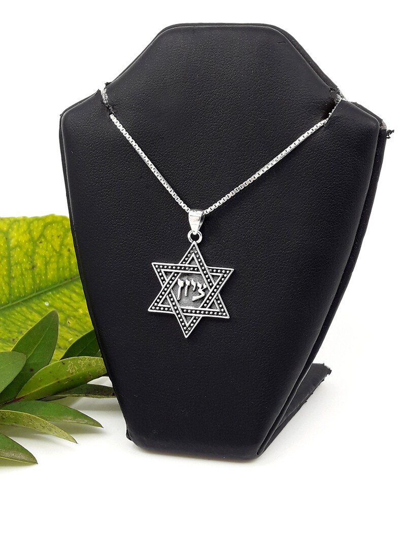 Puede incluir: Un collar de cadena de plata con un colgante de plata de la Estrella de David. El colgante tiene un dise&ntilde;o de esmalte negro y la palabra hebrea "Chai" inscrita en su interior.