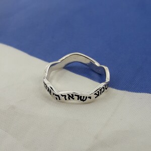 May include: A silver ring with a wavy band and Hebrew text inscribed on the outside.
