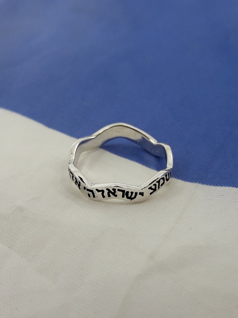 May include: A silver ring with a wavy band and Hebrew text inscribed on the outside.
