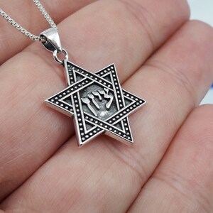 Puede incluir: Un collar con un colgante de plata en forma de Estrella de David con una inscripci&oacute;n hebrea dentro de la estrella. El colgante est&aacute; en una cadena de plata.