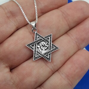 Puede incluir: Un collar de cadena de plata con un colgante de Estrella de David de plata que presenta la palabra hebrea "Chai" en el centro.