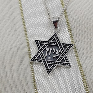 Puede incluir: Un collar de cadena de plata con un colgante de estrella de David de plata. El colgante tiene un acabado de esmalte negro y la palabra hebrea "Chai" inscrita en el centro.