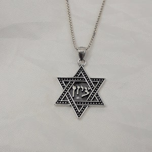 Puede incluir: Un collar de cadena de plata con un colgante de plata en forma de estrella de seis puntas con la palabra hebrea "Chai" inscrita en su interior.