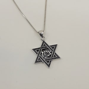 Puede incluir: Un collar de cadena de plata con un colgante de estrella de David de plata. El colgante tiene un acabado de esmalte negro y la palabra hebrea "Chai" inscrita en &eacute;l.