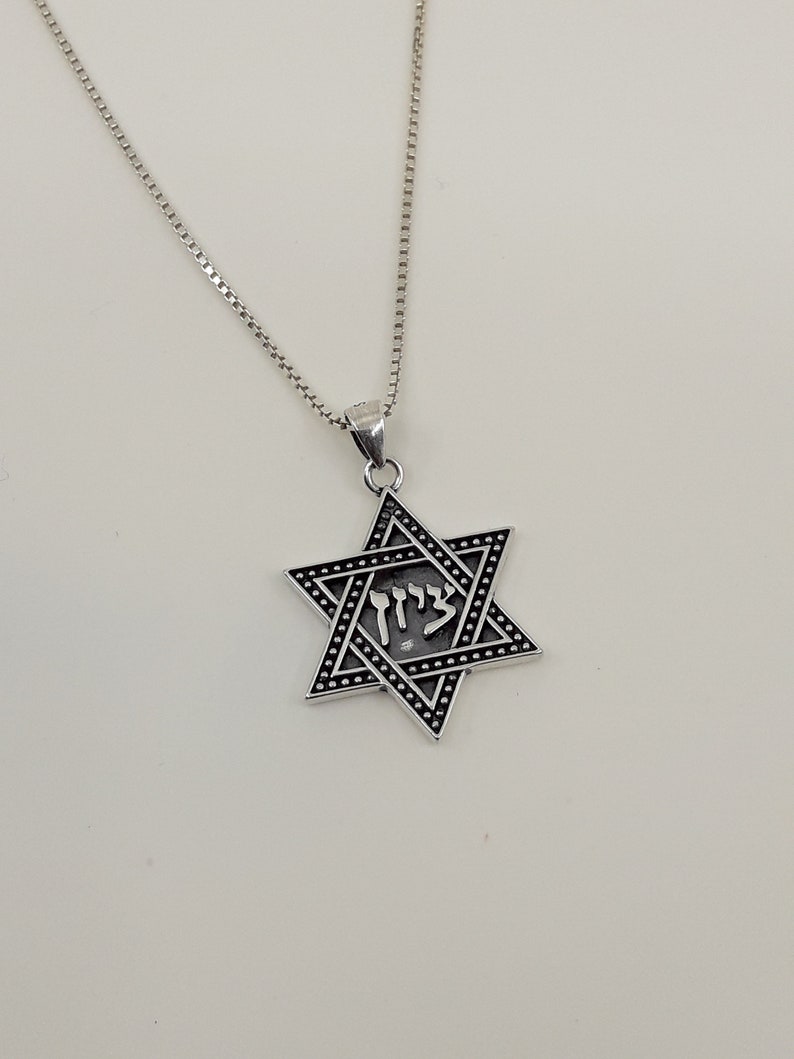 Puede incluir: Un collar de cadena de plata con un colgante de estrella de David de plata. El colgante tiene un acabado de esmalte negro y la palabra hebrea "Chai" inscrita en &eacute;l.