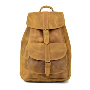 Puede incluir: Una mochila de cuero marrón con un bolsillo frontal grande y dos hebillas ajustables. La mochila tiene un aspecto desgastado y está hecha de cuero de alta calidad.