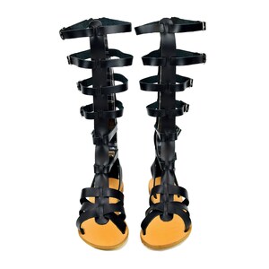 Peut inclure: Une paire de sandales gladiateur en cuir noir avec plusieurs lani&egrave;res et boucles. Les sandales ont une semelle en cuir marron et une pointe ferm&eacute;e.