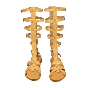 Peut inclure: Une paire de sandales gladiateur en cuir beige avec plusieurs lani&egrave;res et boucles. Les sandales ont une pointe ferm&eacute;e et un talon haut.