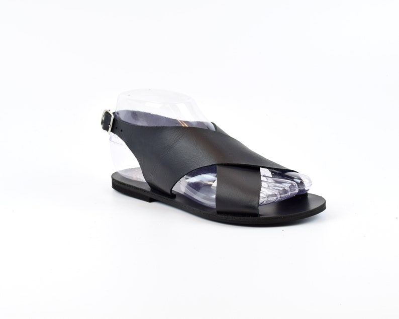 Puede incluir: Sandalias de cuero negro con un dise&ntilde;o de tiras cruzadas y una tira para el tobillo con cierre de hebilla.