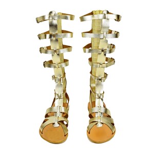 Peut inclure: Une paire de sandales gladiateur dor&eacute;es &agrave; plusieurs lani&egrave;res et boucles. Les sandales ont une semelle en cuir marron.