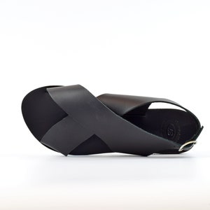 Puede incluir: Sandalias de cuero negro con un dise&ntilde;o de tiras cruzadas y un cierre de hebilla.