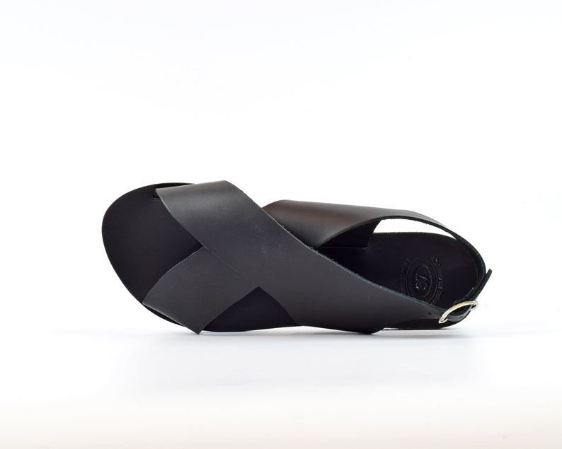 Puede incluir: Sandalias de cuero negro con un dise&ntilde;o de tiras cruzadas y un cierre de hebilla.