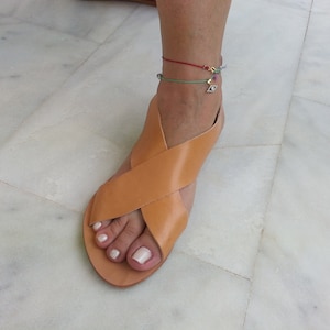 Puede incluir: Sandalias de cuero color canela con un dise&ntilde;o de tiras cruzadas. Las sandalias tienen la punta abierta y una suela plana.