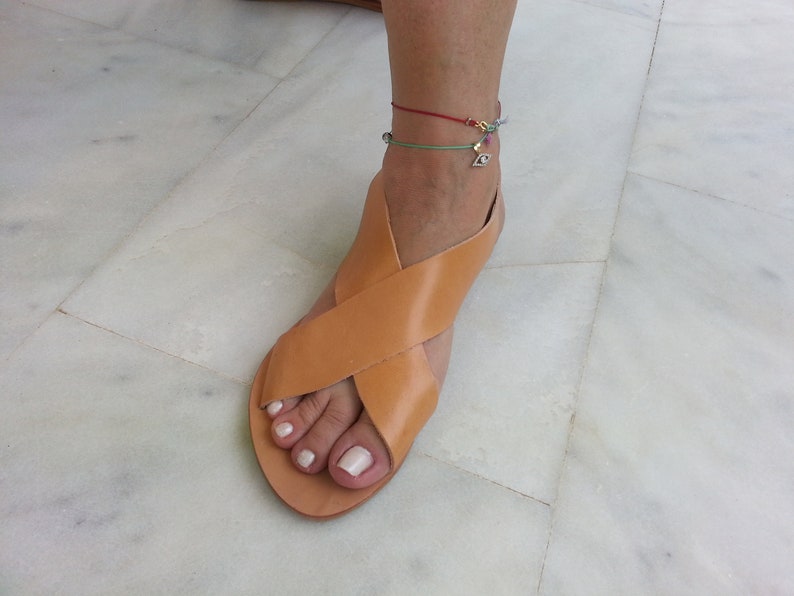 Puede incluir: Sandalias de cuero color canela con un dise&ntilde;o de tiras cruzadas. Las sandalias tienen la punta abierta y una suela plana.