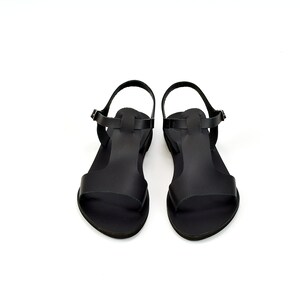Peut inclure: Une paire de sandales en cuir noir avec une bride en T. Les sandales ont une fermeture &agrave; boucle et une semelle plate.