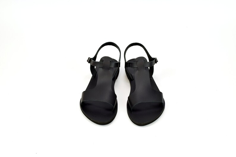 Peut inclure: Une paire de sandales en cuir noir avec une bride en T. Les sandales ont une fermeture &agrave; boucle et une semelle plate.