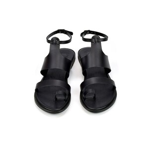 May include: A pair of black leather sandals with ankle straps and toe loops.