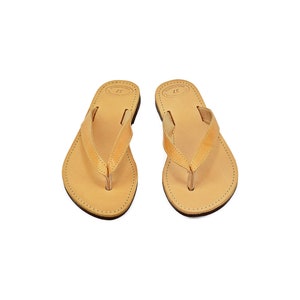 May include: A pair of tan leather flip-flops with a simple design.