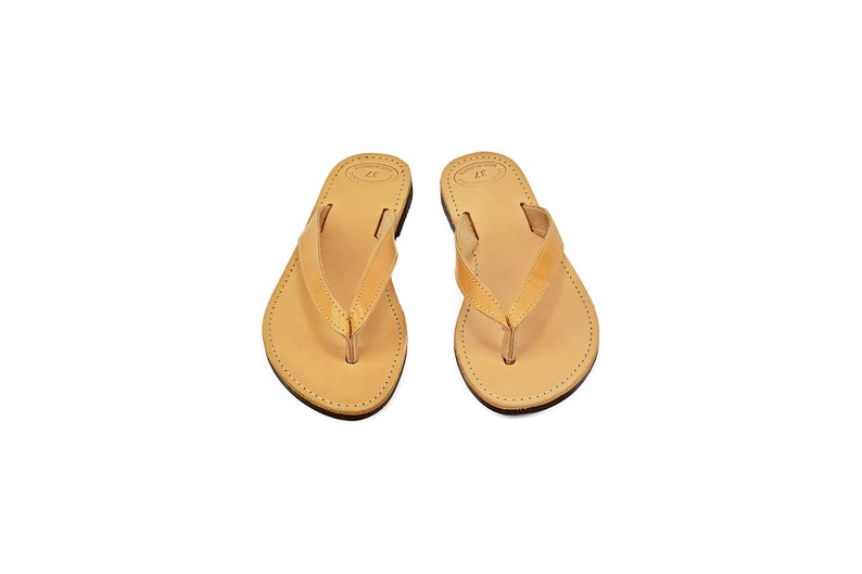 May include: A pair of tan leather flip-flops with a simple design.