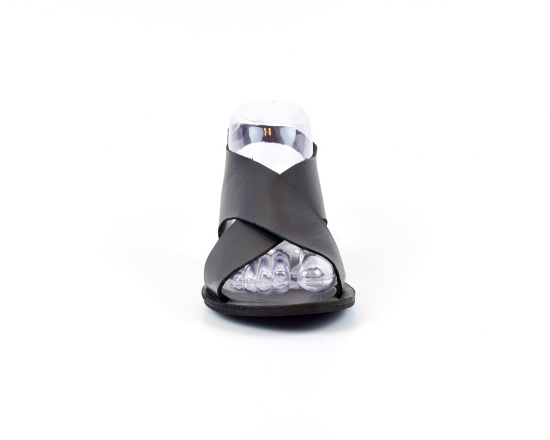Puede incluir: Sandalias de cuero negro con un dise&ntilde;o de tiras cruzadas. Las sandalias tienen una suela plana y un dedo del pie abierto.