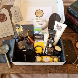 May include: A gift box containing a Wilkinson Sword razor, Bulldog skincare, Sadoer cream, Ferrero Rocher chocolates, a beaded bracelet, a gold pen, a small candle, a magnifying glass, and a compass. Includes tags labelled The Gentleman's Mystery Bundle.