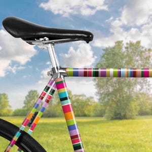 Può includere: Un telaio di bicicletta colorato con una sella nera. Il telaio è decorato con strisce rosa, viola, arancio, giallo, verde e blu.