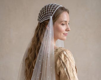Puede incluir: Tocado nupcial con un diseño de red adornado con pequeñas perlas. Un velo blanco transparente con perlas dispersas cae. La mujer lleva una blusa bordada de color dorado. La estética general es elegante y de inspiración vintage.