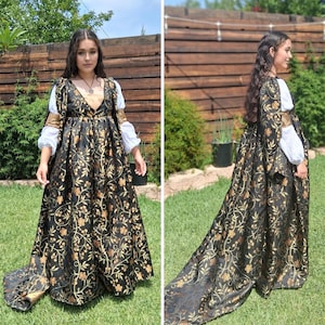Könnte beinhalten: Ein schwarzes und goldenes Kleid im Renaissance-Stil mit langer Schleppe. Das Kleid hat ein Blumenmuster und goldene Akzente auf dem Oberteil und den Ärmeln. Die Ärmel sind weiß mit goldenen Verzierungen. Das Kleid wird im Freien an einem sonnigen Tag getragen.